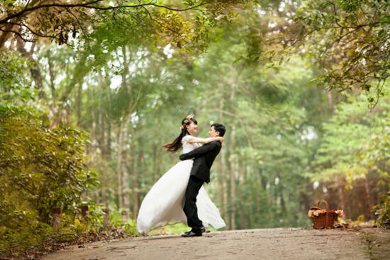A groom hugging his new bride and lifting her into the air in the middle of a road running through a forrest.
